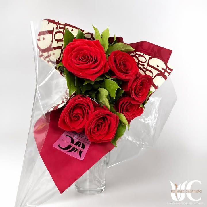 Wrapped bouquet of red roses with greenery and layered decorative paper.