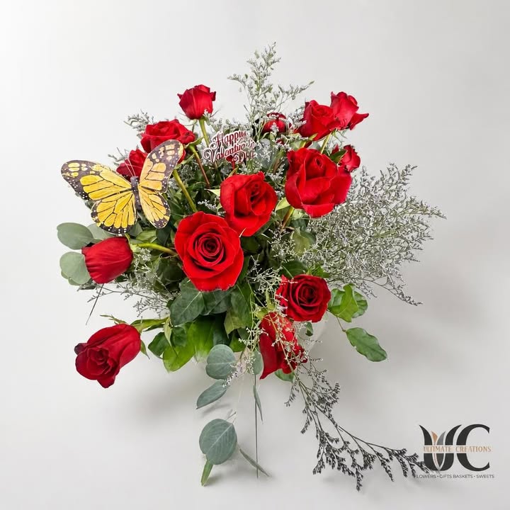 Red rose arrangement with white filler, greenery, butterfly accent, and Valentine’s Day sign.