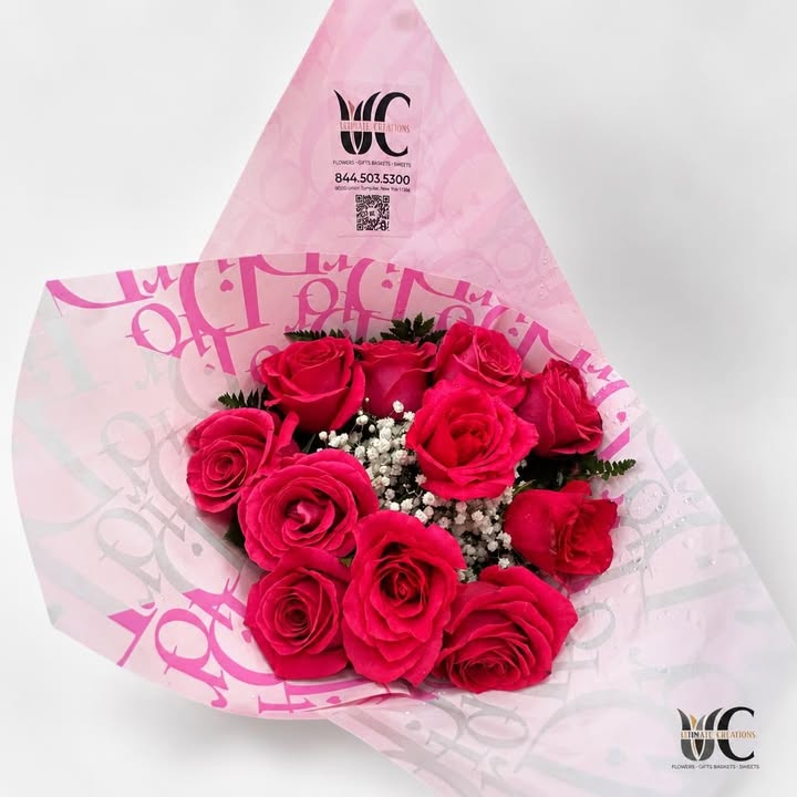 Wrapped bouquet of vivid pink roses with white filler flowers and greenery.