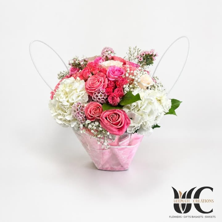Pink and white floral arrangement in a pink handled container against a green foliage wall