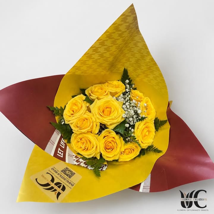 Bouquet of yellow roses with white filler and greenery in yellow and burgundy wrapping.