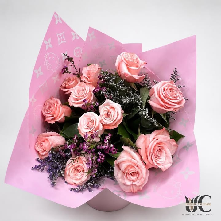 Wrapped bouquet of pink roses with purple and white accents and greenery.
