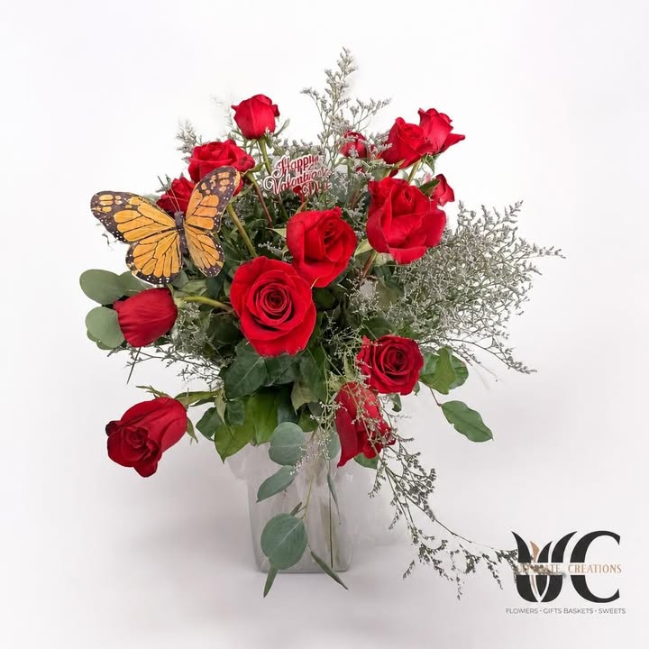 Red rose arrangement with white filler, greenery, butterfly accent, and Valentine’s greeting pick