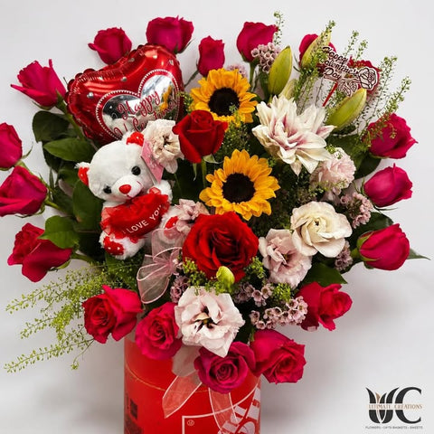 Red and pink flower box with sunflowers, teddy bear, and heart balloon