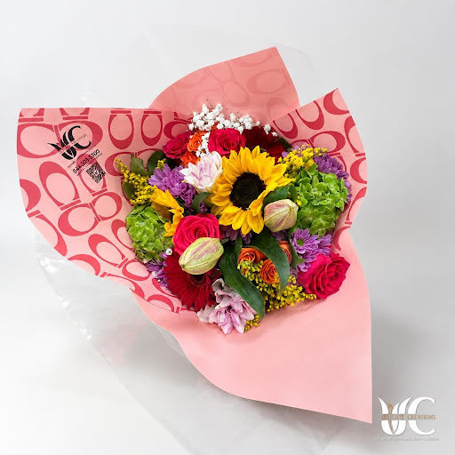 Colorful wrapped bouquet with a sunflower, mixed blooms, and greenery.