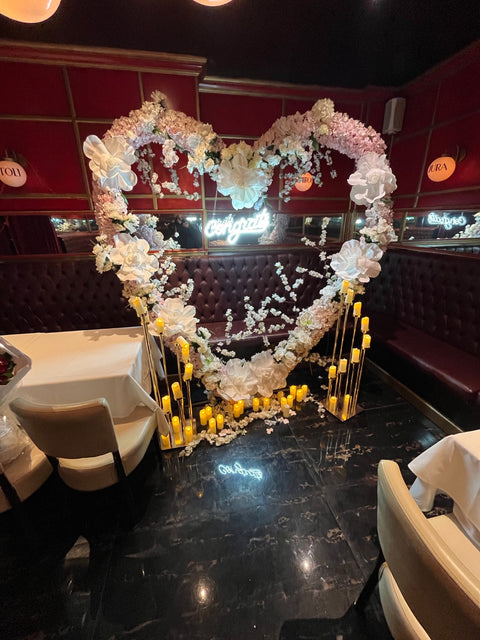 Luxury engagement proposal dinner at Prime Bistro in Five Towns with a white and blush floral heart backdrop and candlelight, styled by Ultimate Creations NY.