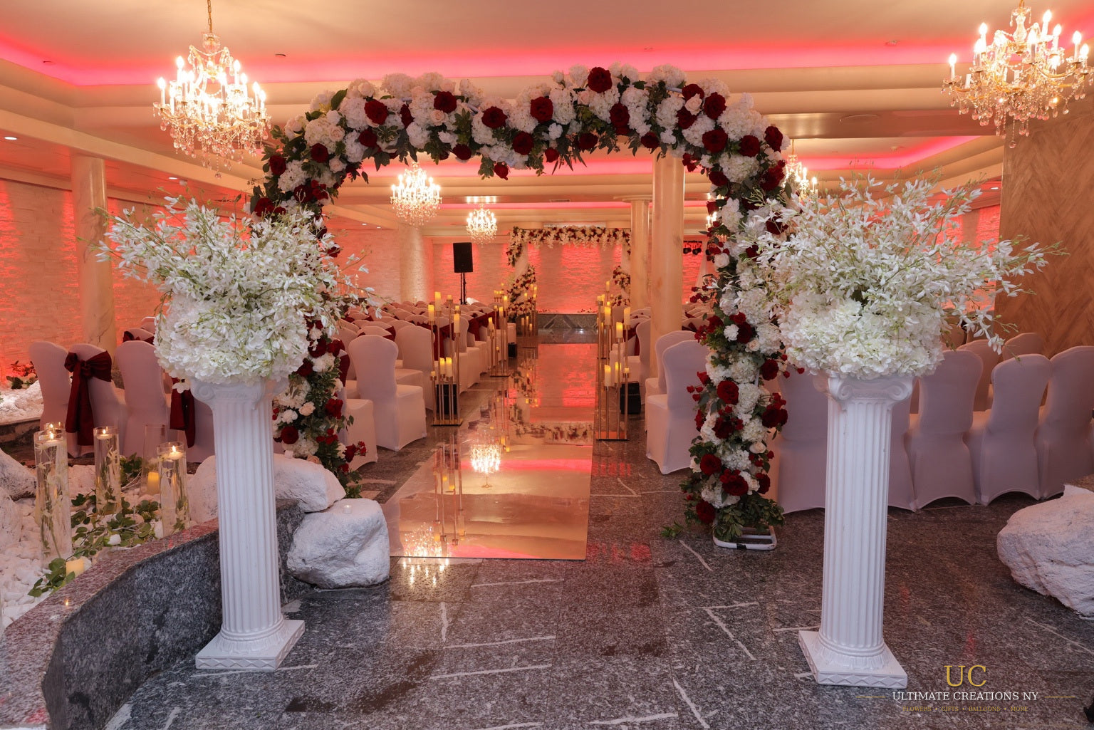N&E wedding ceremony aisle at Floral Terrace with a red and white floral arch, pedestal arrangements and mirrored aisle by Ultimate Creations NY.