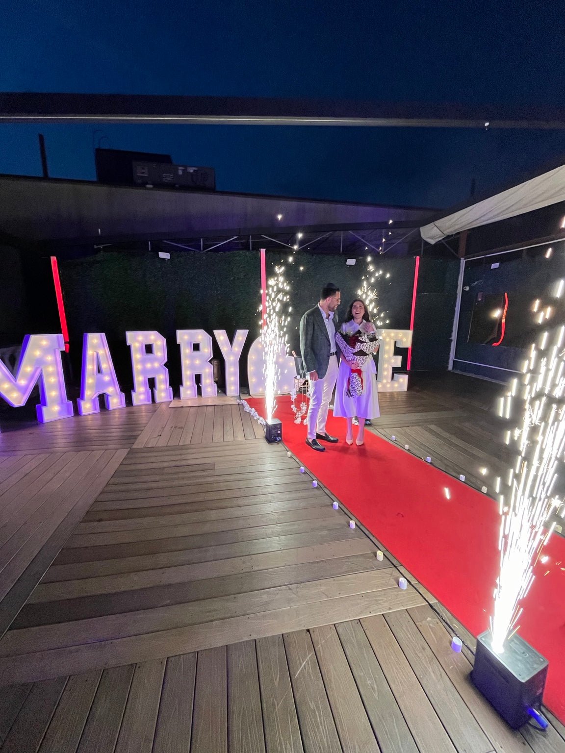 Rooftop engagement proposal at Oligarch Catering Halls in Queens, NY with a red carpet, MARRY ME marquee letters, red rose bouquet and cold sparks by Ultimate Creations NY.