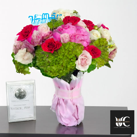 Colorful bouquet of pink and red roses with green hydrangea, wrapped in pink paper.