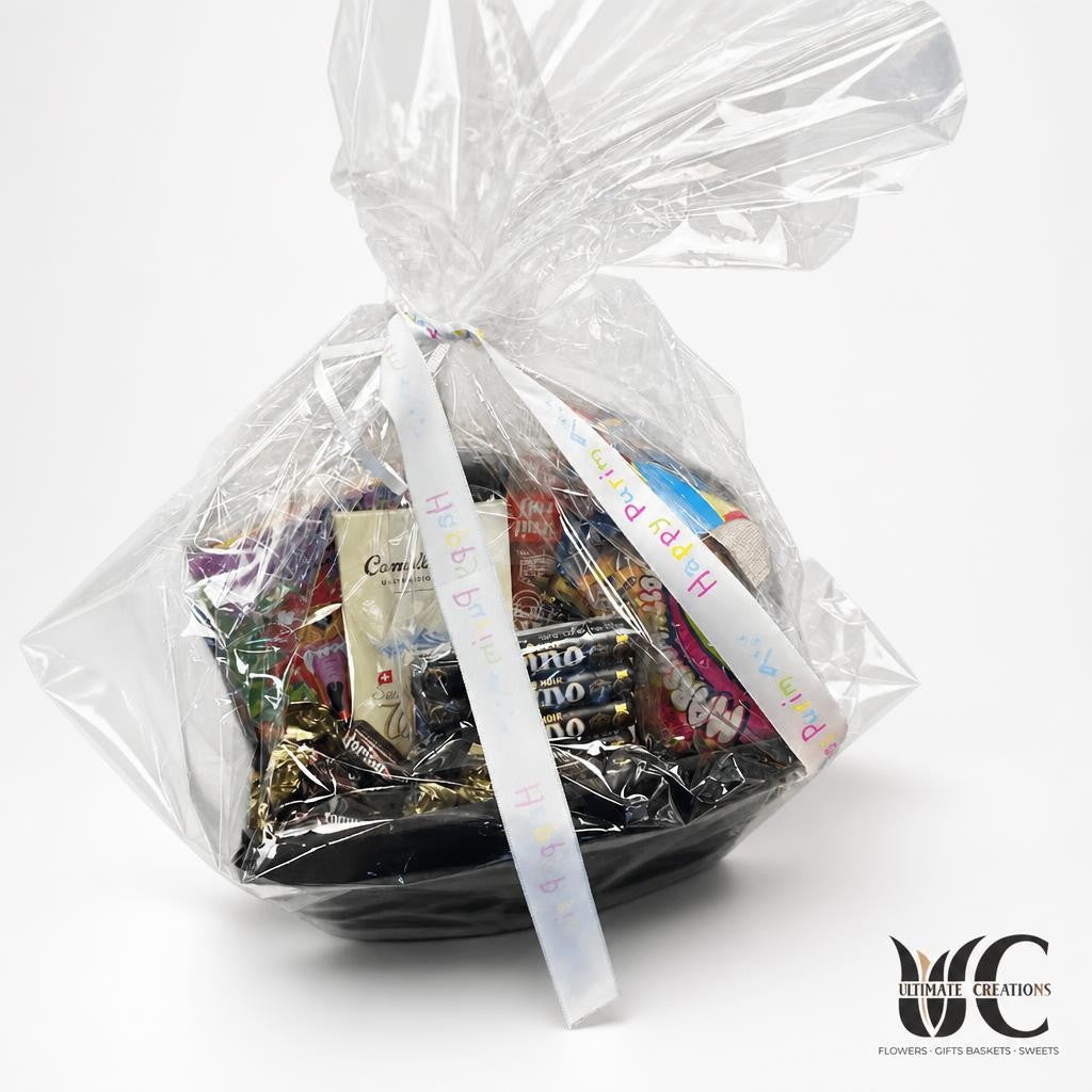 Cellophane-wrapped birthday gift basket filled with assorted packaged chocolates and candies, tied with a multicolored Happy Birthday ribbon.