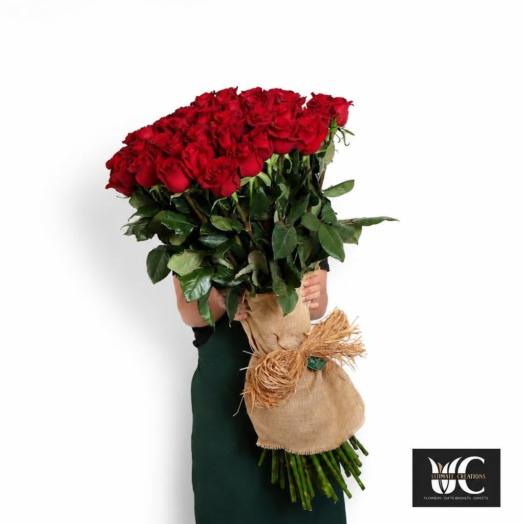 Large bouquet of red roses with green leaves wrapped in burlap and twine.