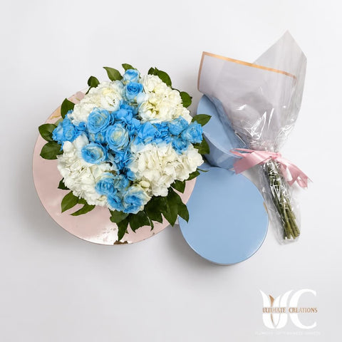 Rounded bouquet of pale blue roses, white flowers, and light blue hydrangea with green leaves, wrapped in pastel paper.