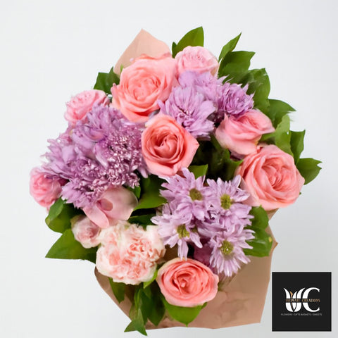 Hand-tied bouquet with pink roses, lavender flowers, and green foliage on a white background.
