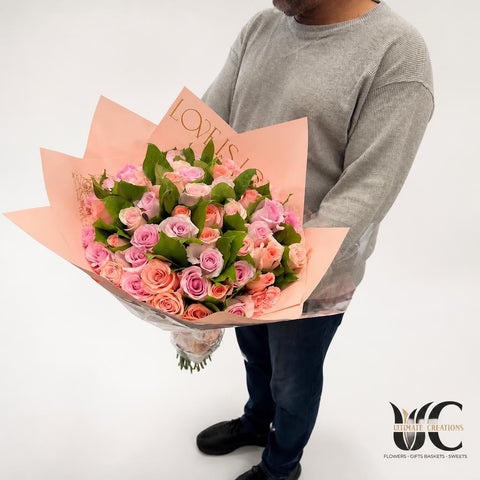Abundant wrapped bouquet of blush pink and peach roses with greenery