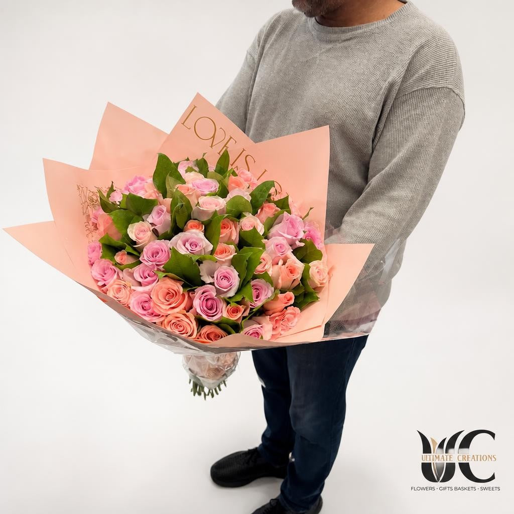 Abundant wrapped bouquet of blush pink and peach roses with greenery