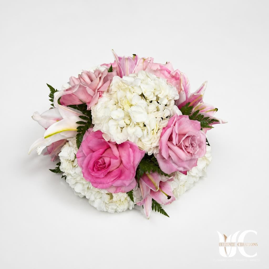 Rounded floral arrangement with pink roses, white hydrangea, pale lilies, and greenery