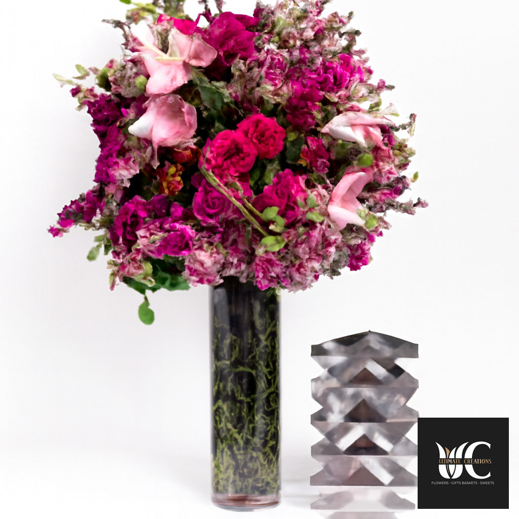Tall vase arrangement with vivid pink and blush flowers in a cylindrical glass vase.