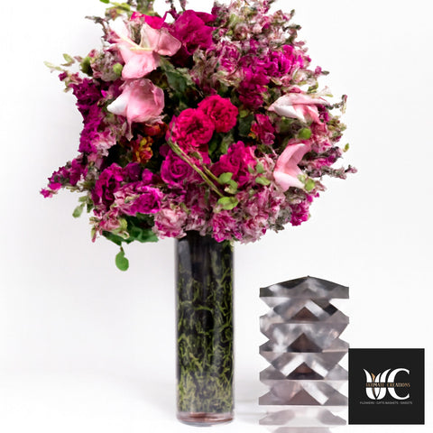 Tall vase arrangement with vivid pink and blush flowers in a cylindrical glass vase.