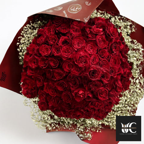 A large bouquet of red roses wrapped in burgundy paper with white baby's breath around the edges.