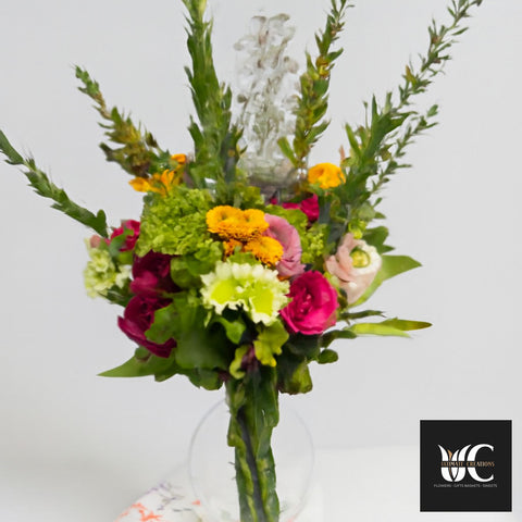 Tall mixed flower arrangement in a clear vase with green foliage, magenta and yellow flowers, and pink accents.