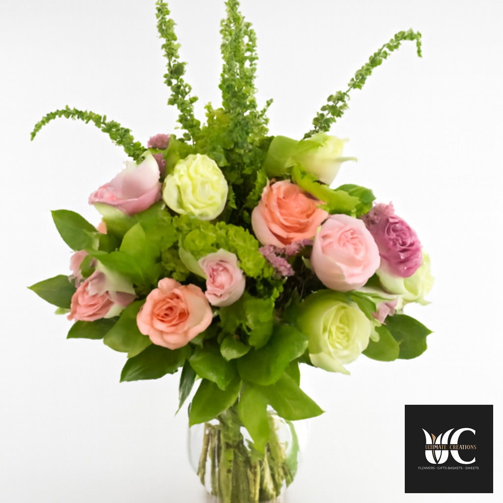 Pastel roses arranged in a lush green bouquet with tall foliage accents in a glass vase.