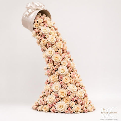 Large white tipped flower box with a cascading diagonal arrangement of ivory and blush roses and small pink flowers on a polished floor.