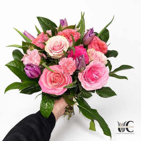 Hand-tied bouquet of pink and purple flowers with roses, carnations, and greenery.