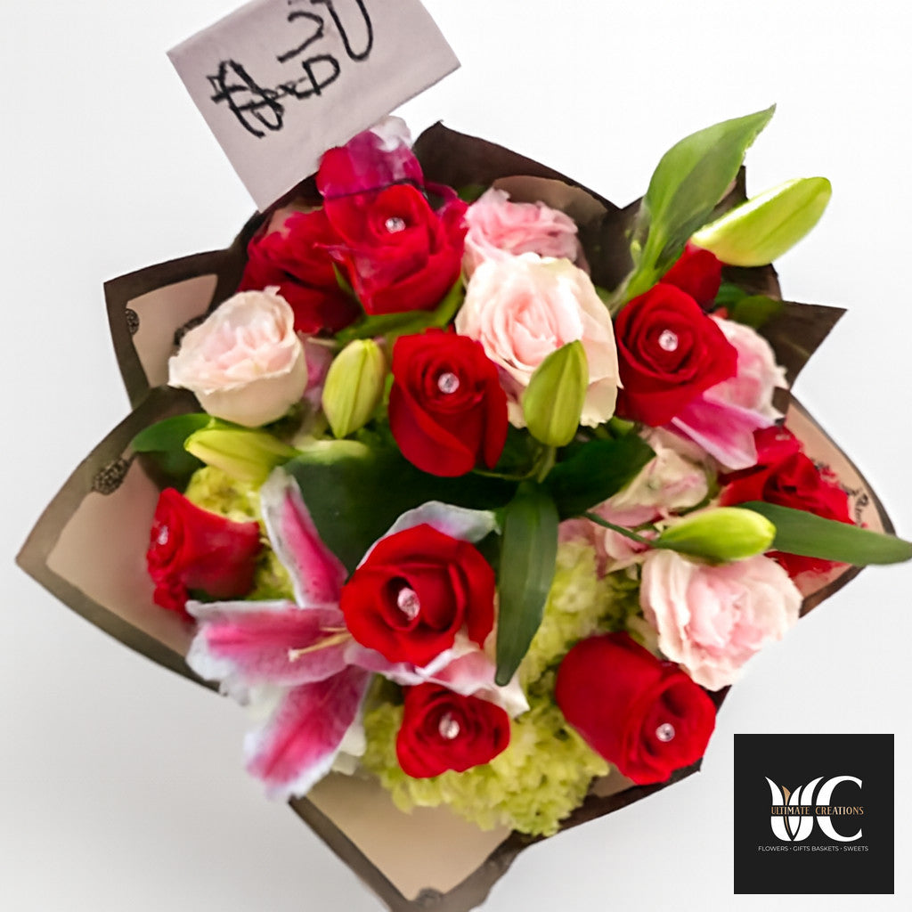 A wrapped bouquet of red and pink flowers with green buds and dark paper wrapping.