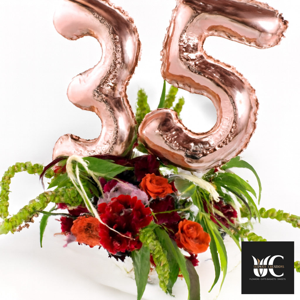 Rose gold number 35 balloons above a lush red, orange, and green floral arrangement.