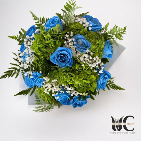 Lush rounded bouquet with blue flowers, green blooms, white filler flowers, and fern foliage.