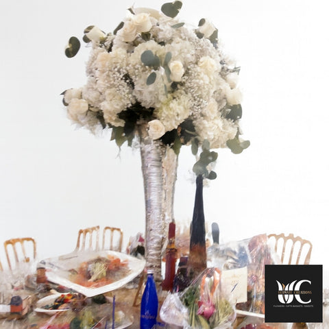 Tall white floral centerpiece with greenery on a decorated table.