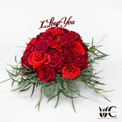 Rounded red rose arrangement with greenery and a Love You topper