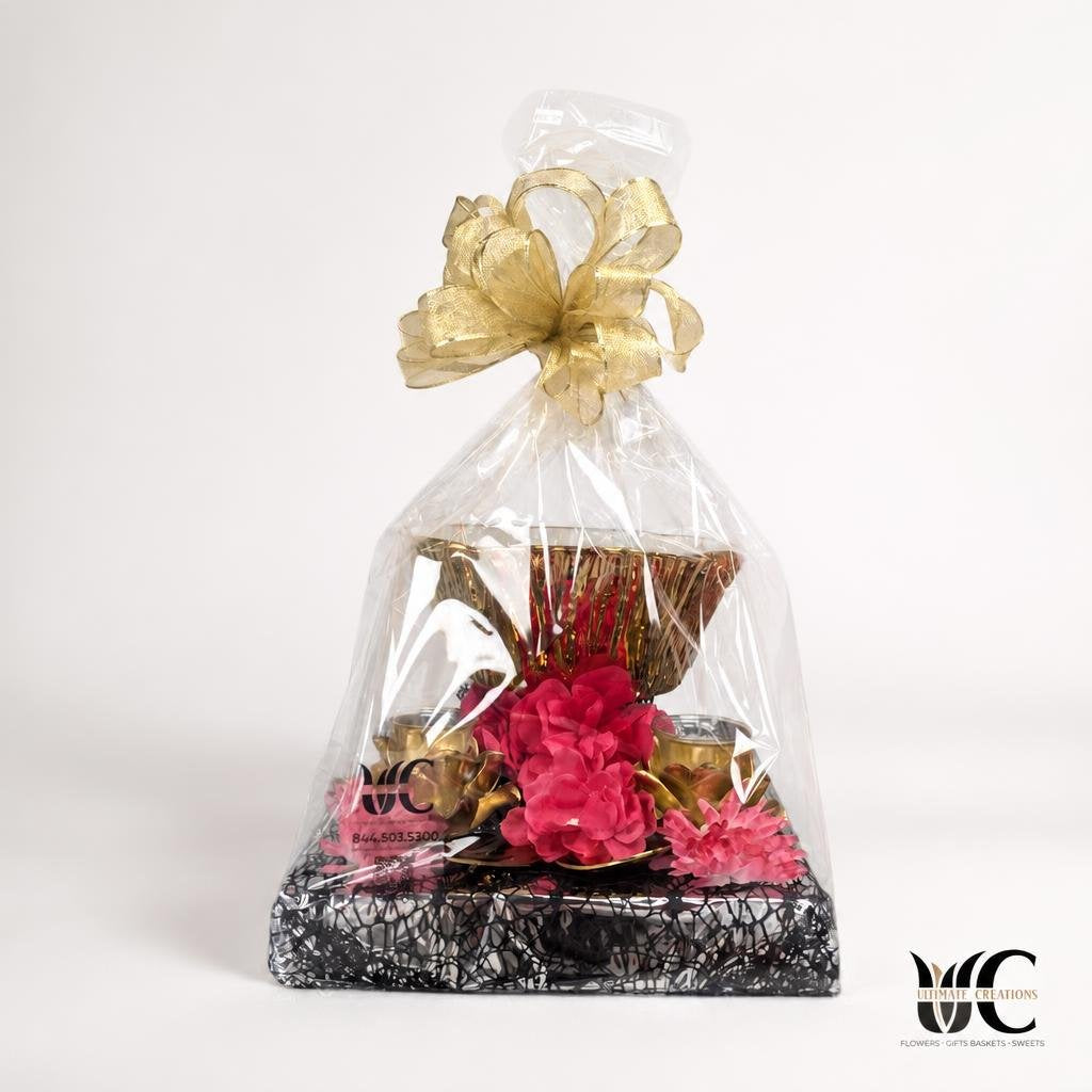 Wrapped gift basket with a large gold bow, pink flowers, and metallic decorative accents.