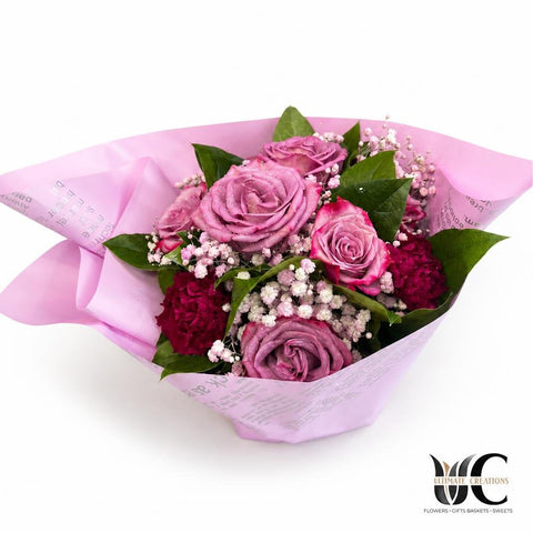 Bouquet of lavender and pink roses with baby’s breath and greenery wrapped in blush pink paper.
