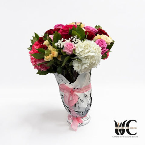 Lush pink, red, and white mixed flower bouquet wrapped in printed paper and ribbon