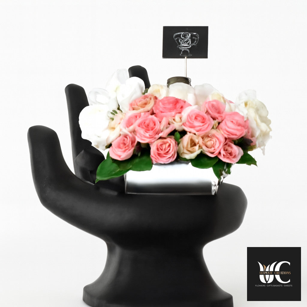 Pink and white rose arrangement on a black sculptural pedestal with a small logo sign above.