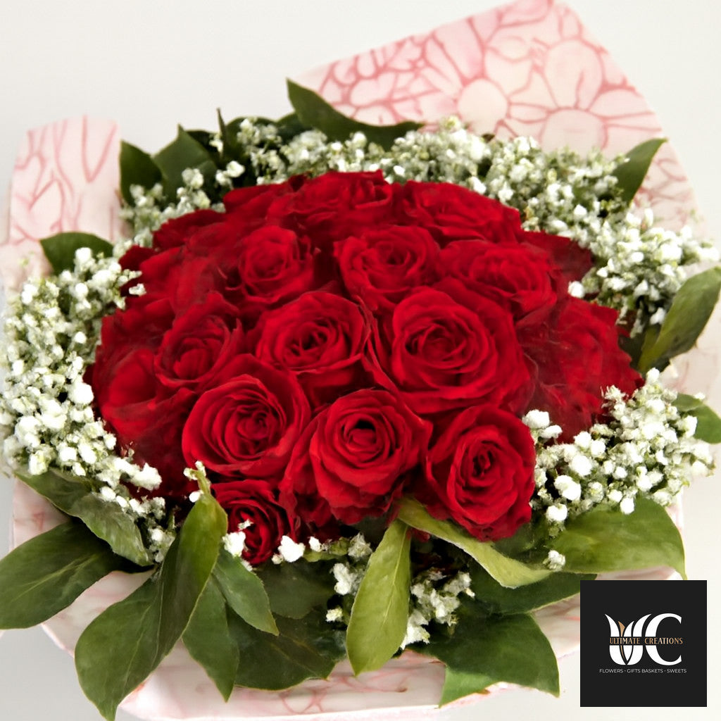 A bouquet of red roses surrounded by baby’s breath and green leaves.