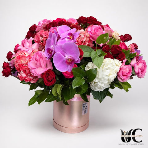 Lush red, pink, white, and purple floral arrangement with orchids in a rose-gold cylindrical vase
