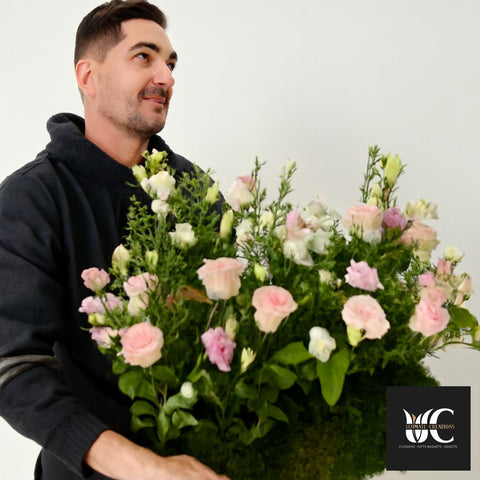 A man holding a large bouquet of pink and white flowers with lush greenery.