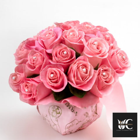 Pink rose arrangement in a decorative hat box with a rounded bouquet shape.