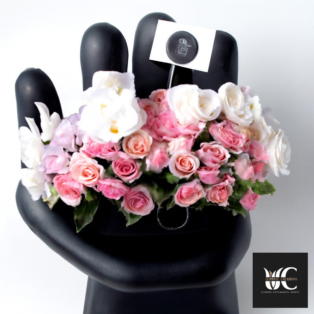 A handheld bouquet of pink and white flowers with green leaves displayed on a black hand mannequin.