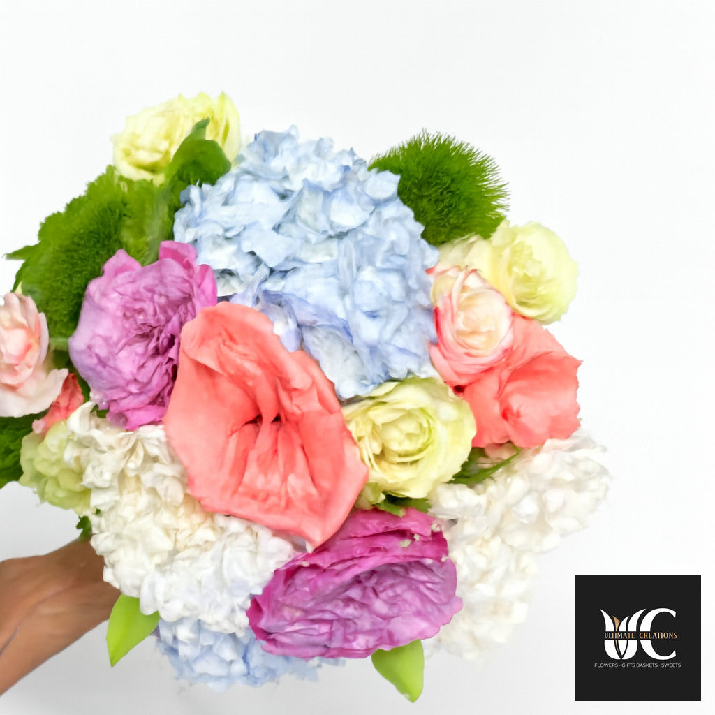 Handheld bouquet of mixed pastel flowers including blue, pink, coral, cream, and green blooms.