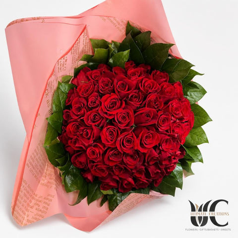 Large bouquet of red roses wrapped in pink paper with green leaves.