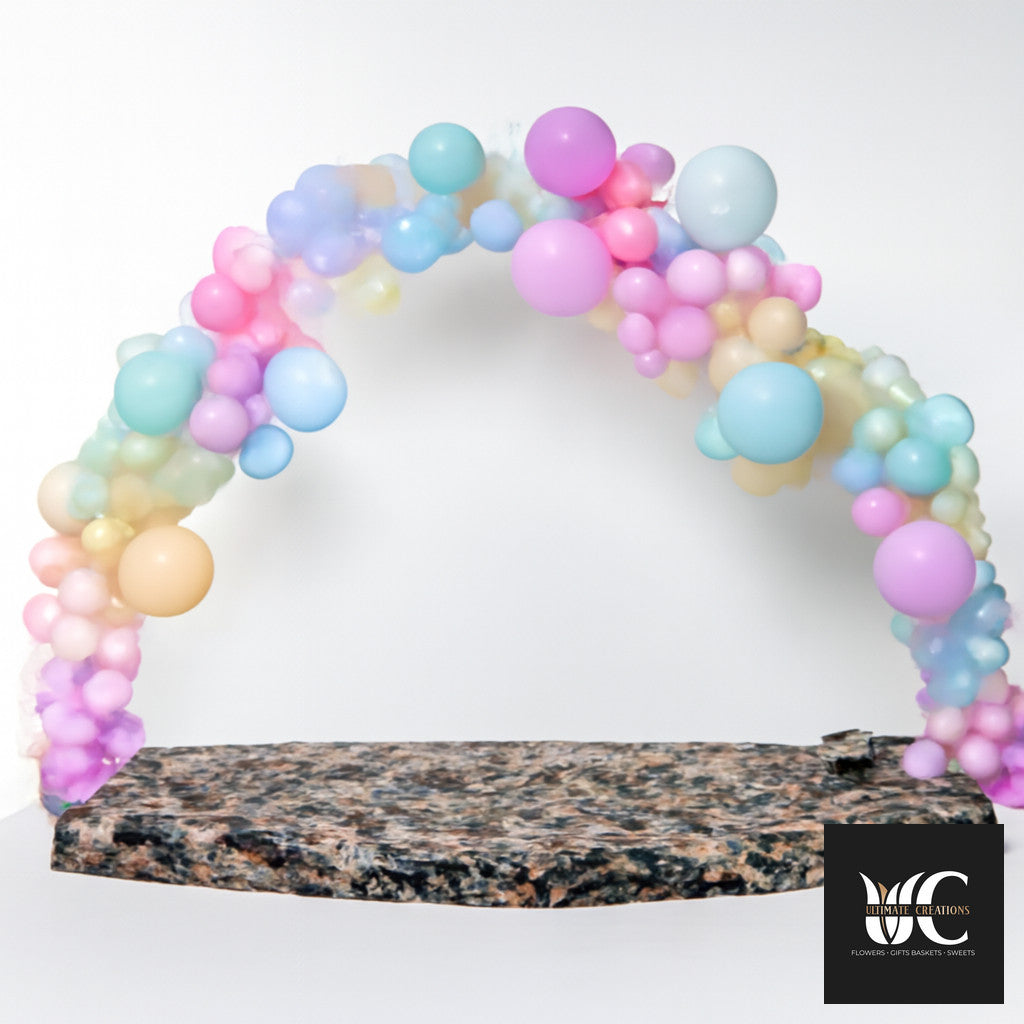 Pastel balloon arch in pink, lavender, blue, mint, and peach over a stone base.