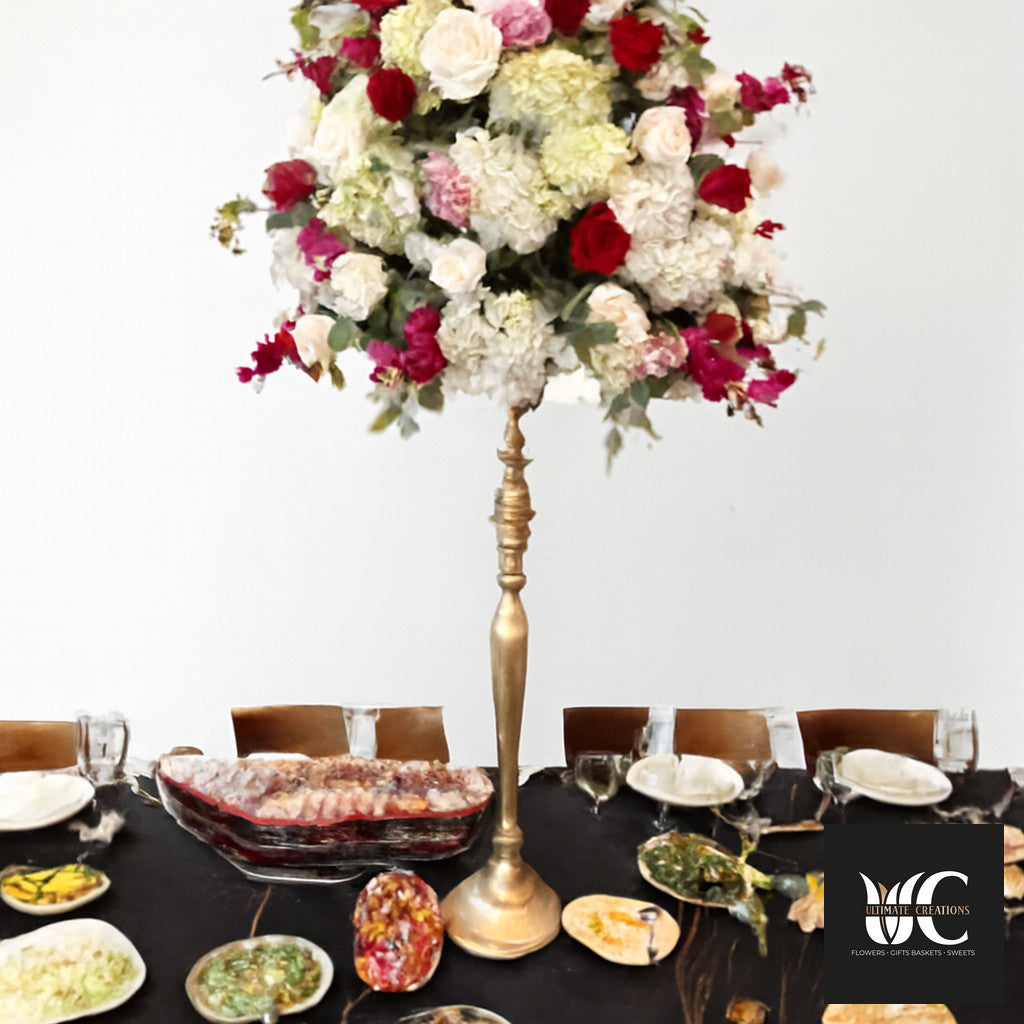 Tall gold pedestal centerpiece with a large mixed floral arrangement above a black-draped banquet table.