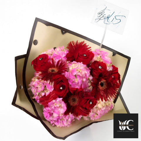 Hand-tied bouquet with red and pink flowers wrapped in cream and black paper.