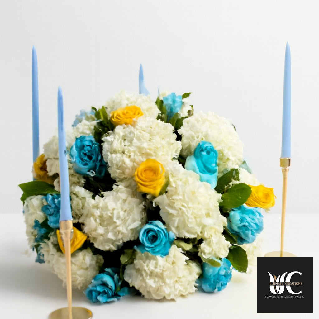 Large white floral centerpiece with blue and yellow flowers and two pale blue taper candles.