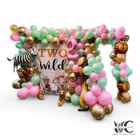 Large pink, mint, lavender, white, bronze, and rose gold balloon garland surrounding a Two Wild backdrop, with zebra, lion, monkey, and other safari animal balloons in a decorated indoor room.