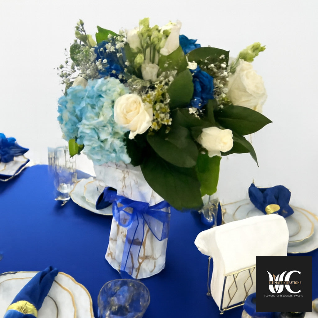 Blue and white floral centerpiece with greenery on a decorated table.