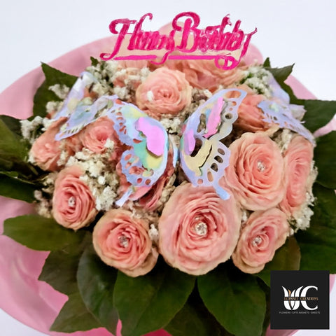 Pink bouquet with layered blooms, baby’s breath, butterfly accents, and a pink topper.